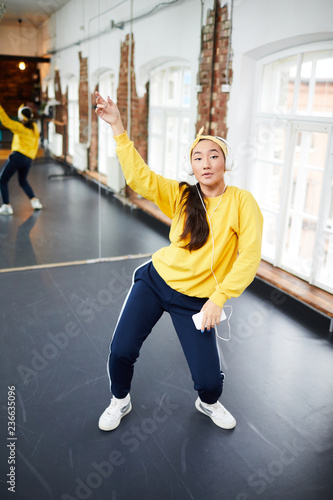 Active young dancer training in studio over music in headphones with large mirror on background