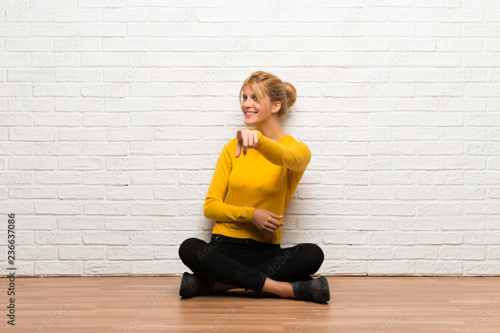 Young girl sitting on the floor points finger at you with a confident expression Young girl sitting on the floor points finger at you with a confident expression
