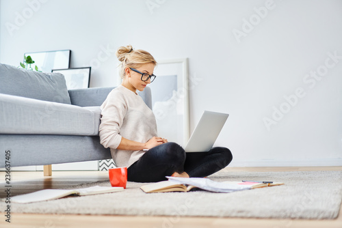 Photography Young woman sitting on floor at home working with laptop and documents