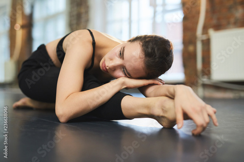 Young female dancer lying on her stretched leg during relax exercise on the floor