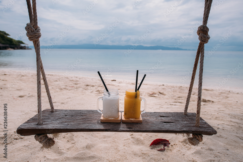 Fruit cocktails stand on a wooden swing overlooking a sandy tropical beach. Healthy food Fruit cocktails stand on a wooden swing overlooking a sandy tropical beach. Healthy food