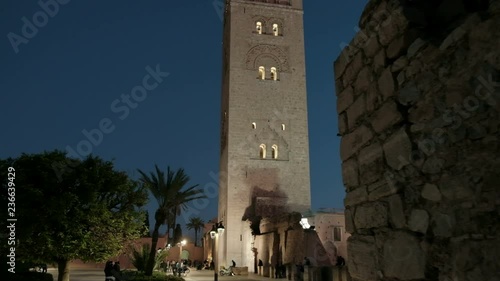 Dusk camera forward push in, tilt up to reveal beautifully lighted low angle view of Koutoubia Mosque minaret in Marrakech, Morocco photo