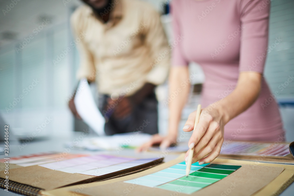Hand of designer with pencil pointing at pale green color in swatch while choosing the most suitable one Hand of designer with pencil pointing at pale green color in swatch while choosing the most suitable one