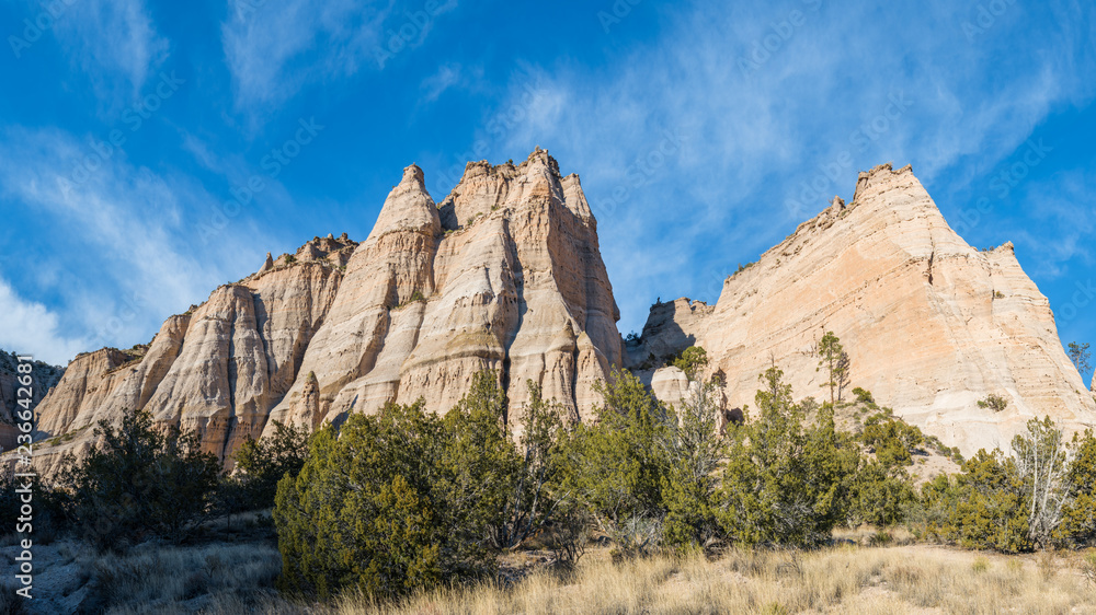 Panorama of steep, sharp peaks and rock formations over a grassy meadow under a blue sky with wispy clouds at Kasha-Katuwe Tent Rocks National Monument