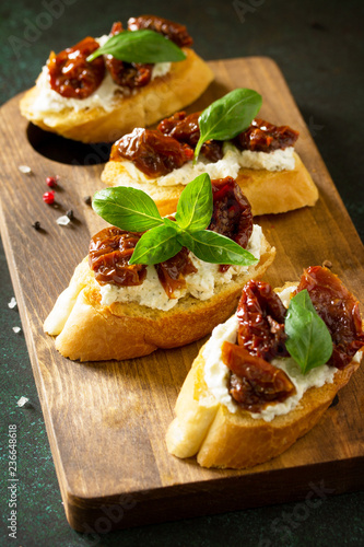 Antipasti snacks for Wine. Brushetta with Soft Cheese and Dried Tomatoes served on a rustic wooden board on a stone table.