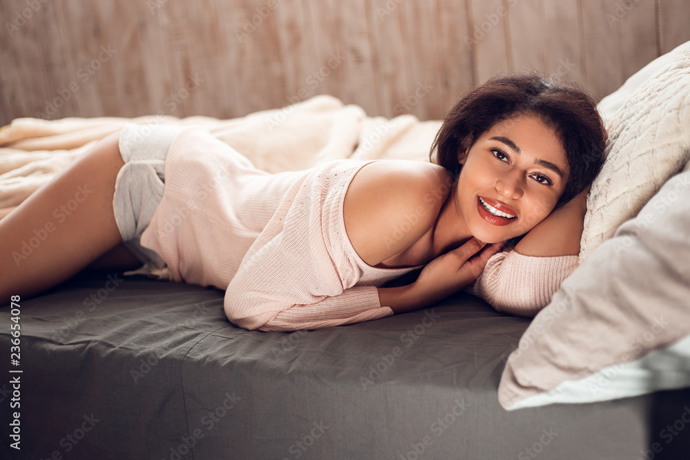 Sleeping beauty. Side view of beautiful young black woman looking at camera with smile while lying down on her bed Sleeping beauty. Side view of beautiful young black woman looking at camera with smile while lying down on her bed