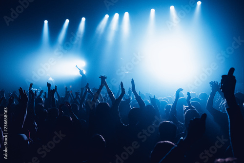silhouettes of concert crowd in front of bright stage lights. Unrecognized people in crowd. Copy space background. Crowd of fans at music festive. Party in nightclub. Sold out concert.