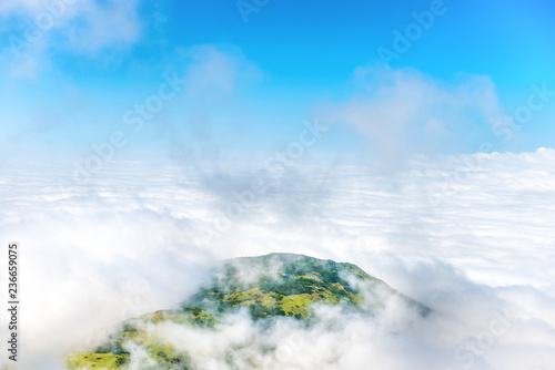 Green mountain peak in white clouds and blue sky