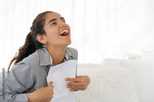 Young woman enjoying good news in writing. The girl reads a letter with good news sitting on the couch. An euphoric girl is happy after reading good news in a written letter, approving a loan.