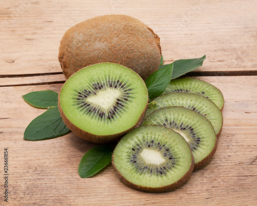Kiwi fruit whole and sliced on a wooden table.