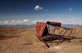 Old rusty metal construction on highland steppe valley with dry yellow grass on the background of rocky mountains under clear sky