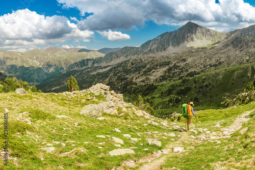 Happy woman hiker travels in Pyrenees Mountains in Andorra and Spain. Nordic walking, recreation and trekking along GR11 path trail