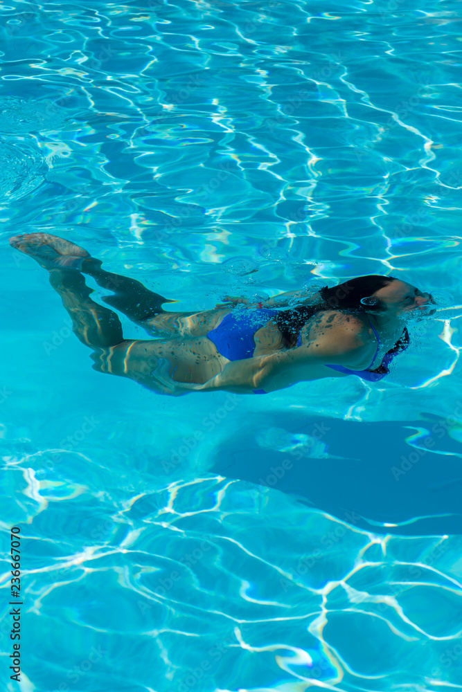 Woman with swimsuit swimming on a blue water pool. Underwater woman portrait with blue bikini in swimming pool. vertical photo