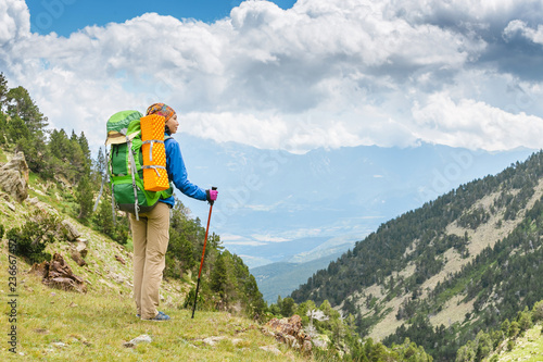 Happy woman hiker travels in Pyrenees Mountains in Andorra and Spain. Nordic walking, recreation and trekking along GR11 path trail