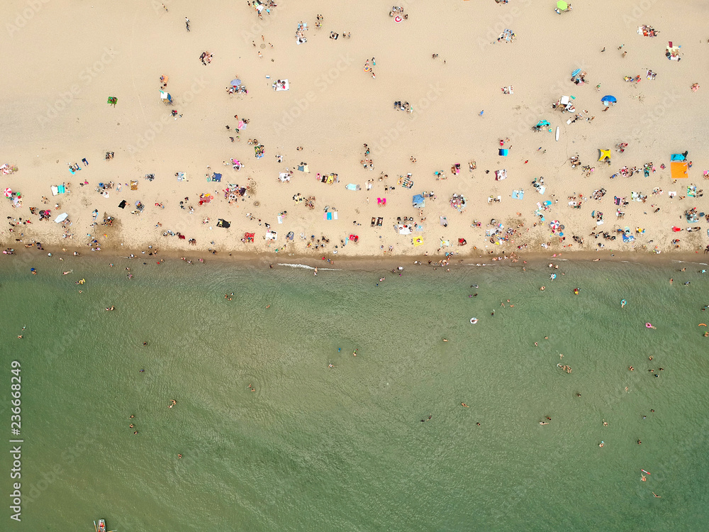 View from above, aerial view of  green North American Canadian water lake with a white beach with beach umbrellas and people, kids and tourists who relax and swim. Ontario.