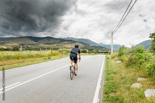 A cyclist riding towards storm clouds above mountains
