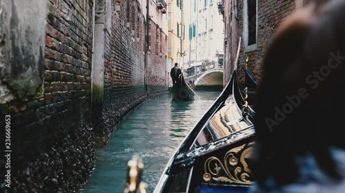 Back view of senior woman enjoying beautiful gondola excursion tour on narrow Venice canal during retirement vacation.