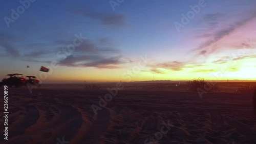 Dune buggies driving by as the sun is setting in the desert