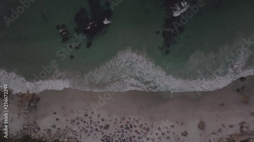 Drone aerial looking down at Cape Town, South Africa beach crowded with people having picnics on colorful picnic rugs at sunset with blue ocean with boulders and seaweed