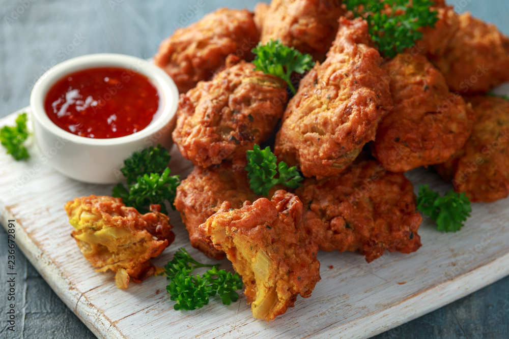 Crispy onion bhajis with sweet chilli sauce on white wooden board