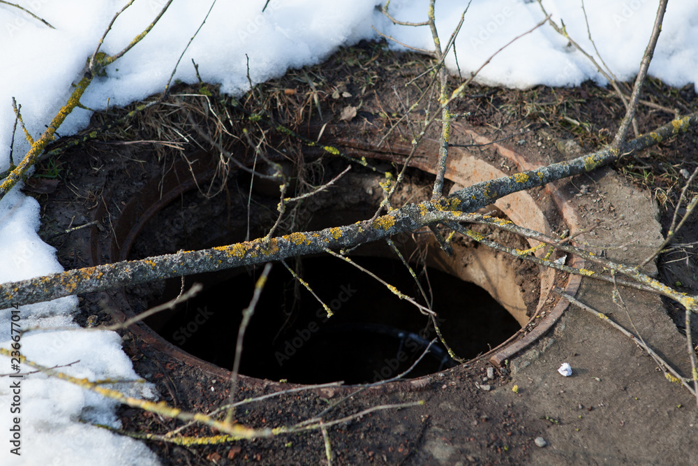 Obraz premium Dangerous manhole without a cover laid wooden planks closeup