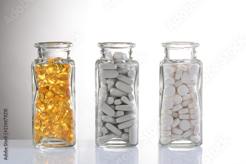 Three glass bottles with different pills on a light gray gradient
