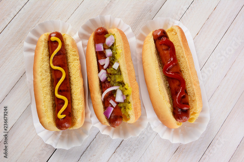Photography Three hot dogs on a wood table with different condiments