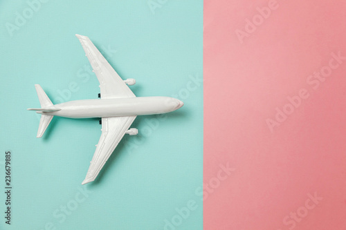 Simply flat lay design miniature toy model plane on blue and pink pastel colorful paper trendy geometric background. Travel by plane vacation summer weekend sea adventure trip concept