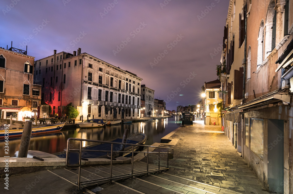 A canal - street with boats in Venice at night, Italy.