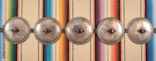 Large Diameter Concho, Navajo First Phase Style Silver Concha Belt. Sterling Silver with a leather belt with intricate craftmanship, on a colorful woven textile background. photo