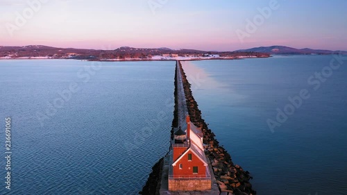 Aerial footage flying towards shore past the brick lighthouse at the end of a snow dusted rocky breakwater in Rockland Maine at sunrise photo