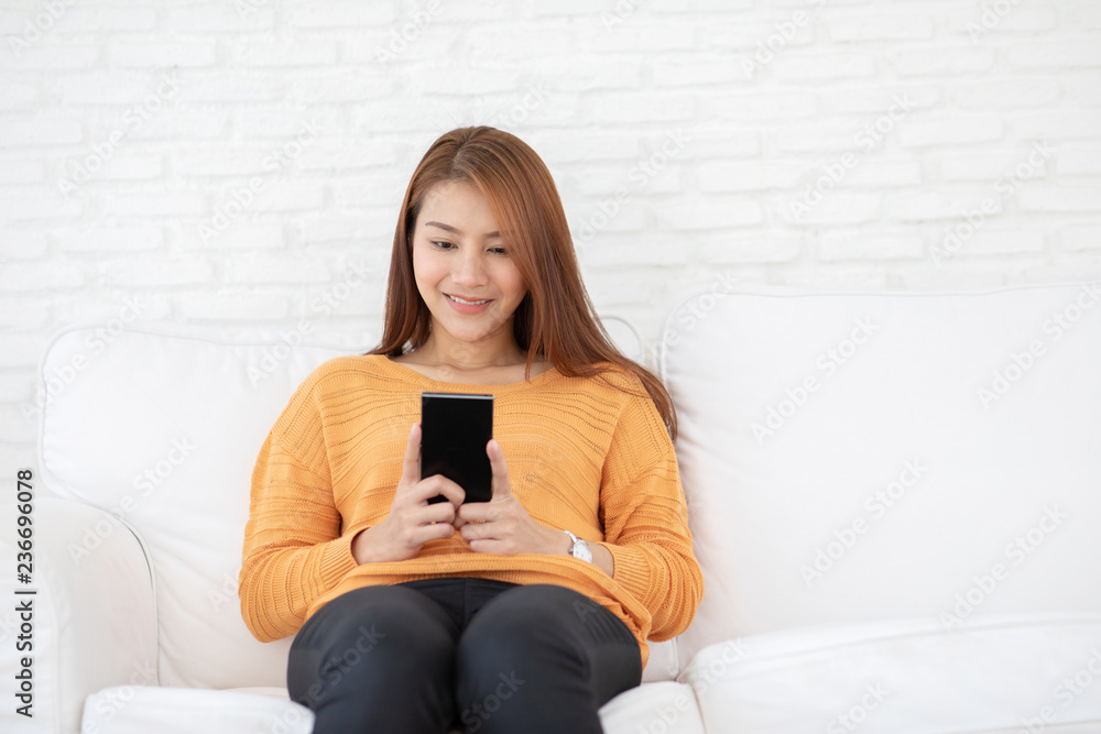 Beautiful Attractive Asian woman sitting on white sofa using smartphone in living room smile and happiness with social media and shopping online,Lifestyle in Holidays Concept Beautiful Attractive Asian woman sitting on white sofa using smartphone in living room smile and happiness with social media and shopping online,Lifestyle in Holidays Concept