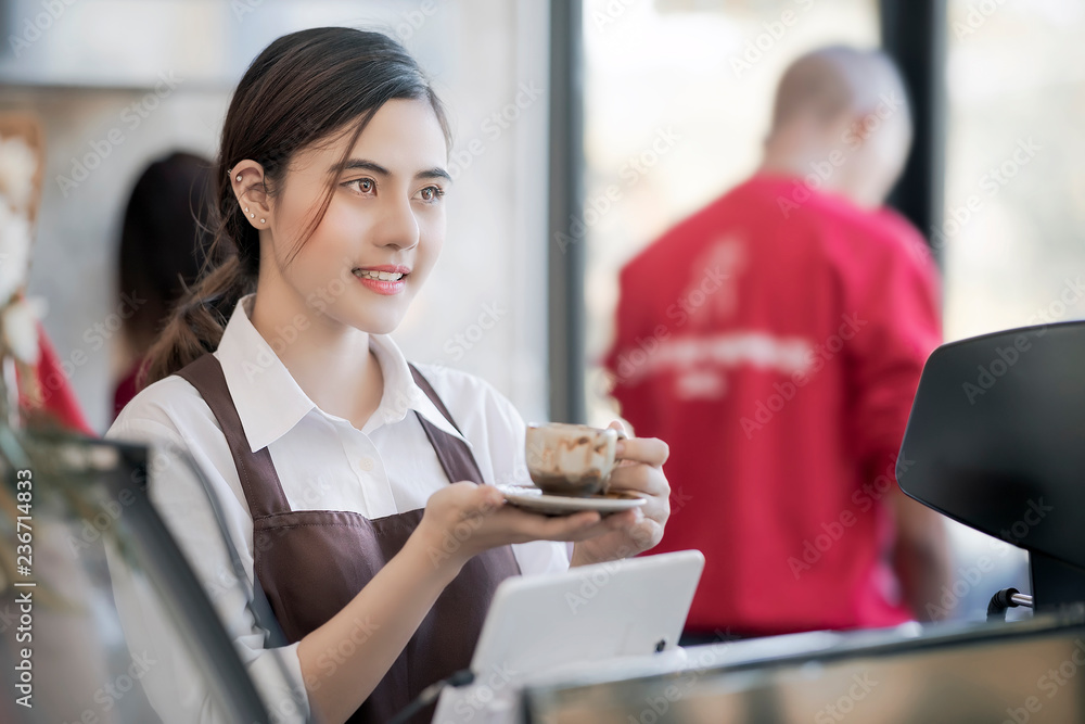 beautiful barista wearing brown apron holding hot coffee cup served to customer with smiling face at bar counter,Cafe restaurant service concept