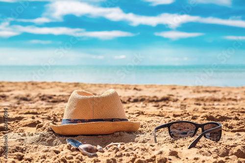 Sunglass and cap on sand against turquoise sea.