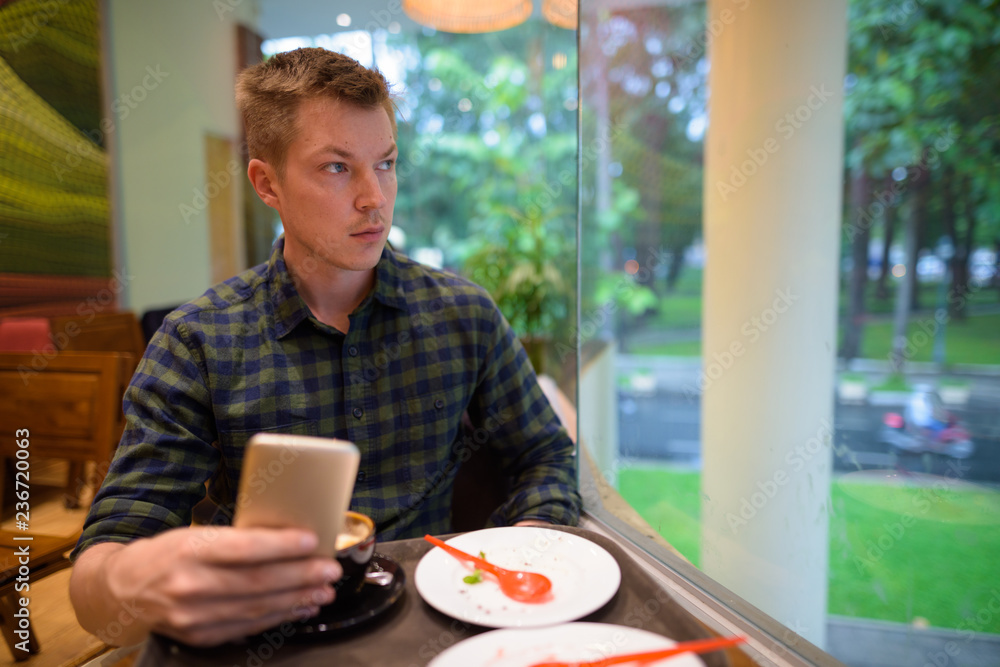 Man sitting in coffee shop while using mobile phone and thinking Man sitting in coffee shop while using mobile phone and thinking