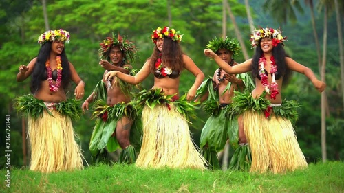 Polynesian men in warrior dress with girls in grass skirts and flower headdress dancing hula style while entertaining barefoot outdoors Tahiti French Polynesia 