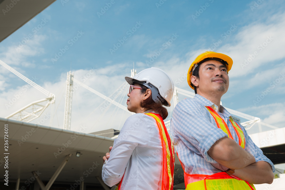 Portrait of two engineers standing near each other in front of white contrustion building look at sky. Portrait of two engineers standing near each other in front of white contrustion building look at sky.