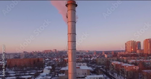 A large boiler room is located in the middle of a snowy city. From her five huge pipes, smoke and steam are pulled out of the air. It all sneaks up with a red sunshine.