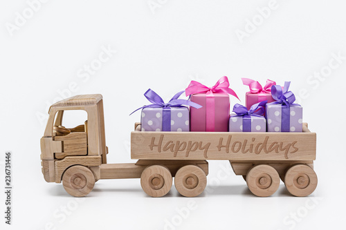 Boxes with gifts in purple with white polka dots and pink paper, carrying toy wooden truck. Holiday concept.
