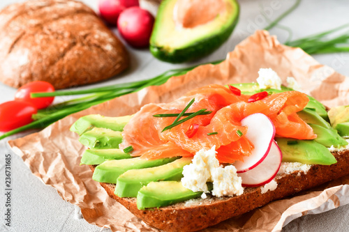 sandwich with avocado and salmon on a light background, green onions and gluten-free grain bread, radishes and tomatoes. concept diet food, copy space, sandwich take away, healthy fast food