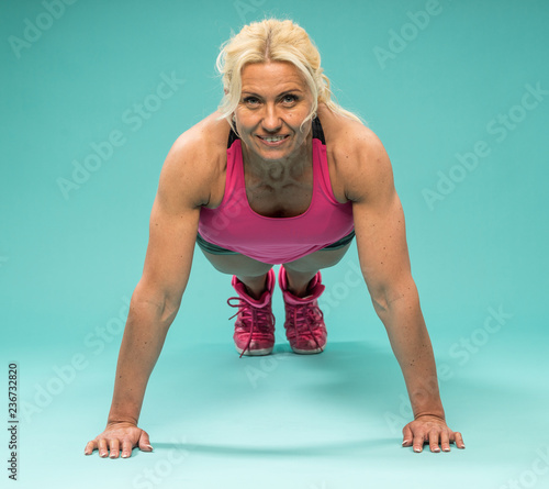 Athletic woman in workout clothes posing in studio. Attractive fitness lady with long blond hair showing her muscles