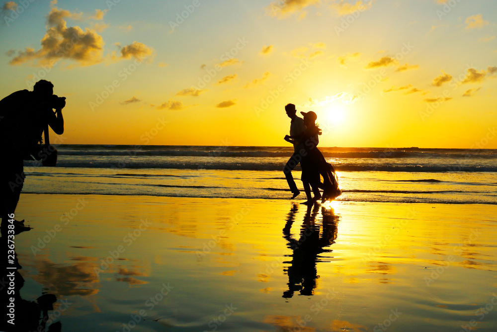 SILHOUETTE OF ROMANTIC COUPLE  WALKING ON THE BEACH  DURING SUNSET DOING PICTURE SHOOTING 