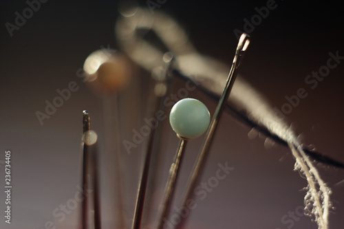 needles with threads and pins stick out in different directions on a dark background, illuminated by the sun