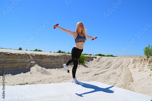 Sporty blonde girl makes swallow on hot sand background.