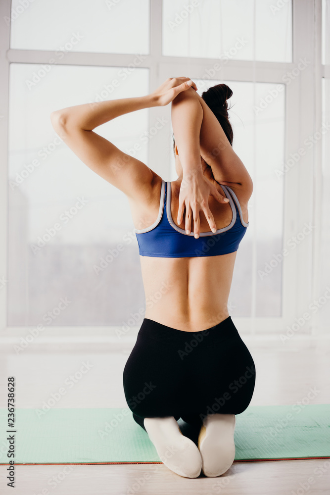 yoga, fitness, sport, active lifestyle, flexibility, healthy spine. Young fit woman stretching arms to warm up before workout in studio, back view