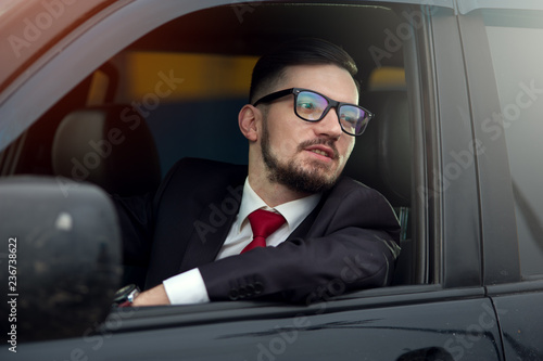 Portrait of successful business man in glasses sitting at the wheel of an expensive car and looking out the door window © pavel_shishkin