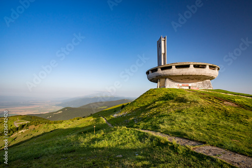 Landscape view of abandoned communist monument, Buzludzha peak, Stara Planina mountain, Bulgaria, early spring morning with clear blue sky and green grass.
