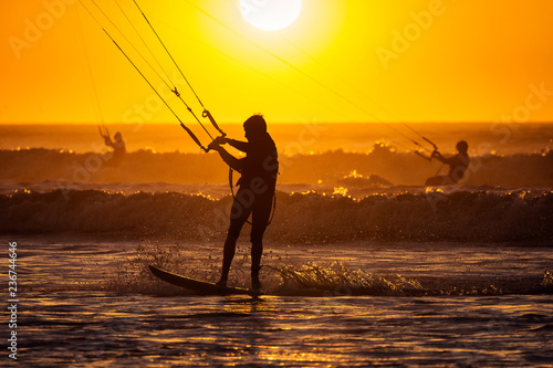 Silhoutte of kitesurfers enjoying big waves at sunset in Essaouira, Morocco. Beautiful landscape in background