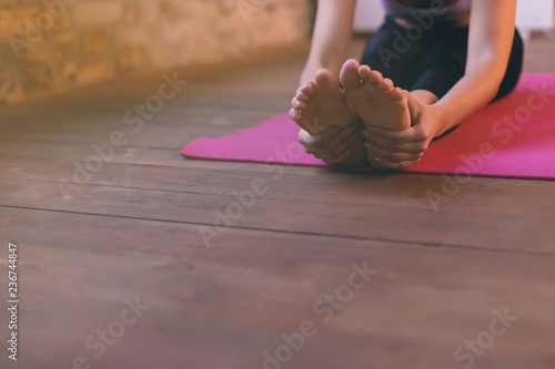 Close-up of a girl doing an asana bending forward with her hands towards her legs. Sitting on the floor on a pink yoga mat.