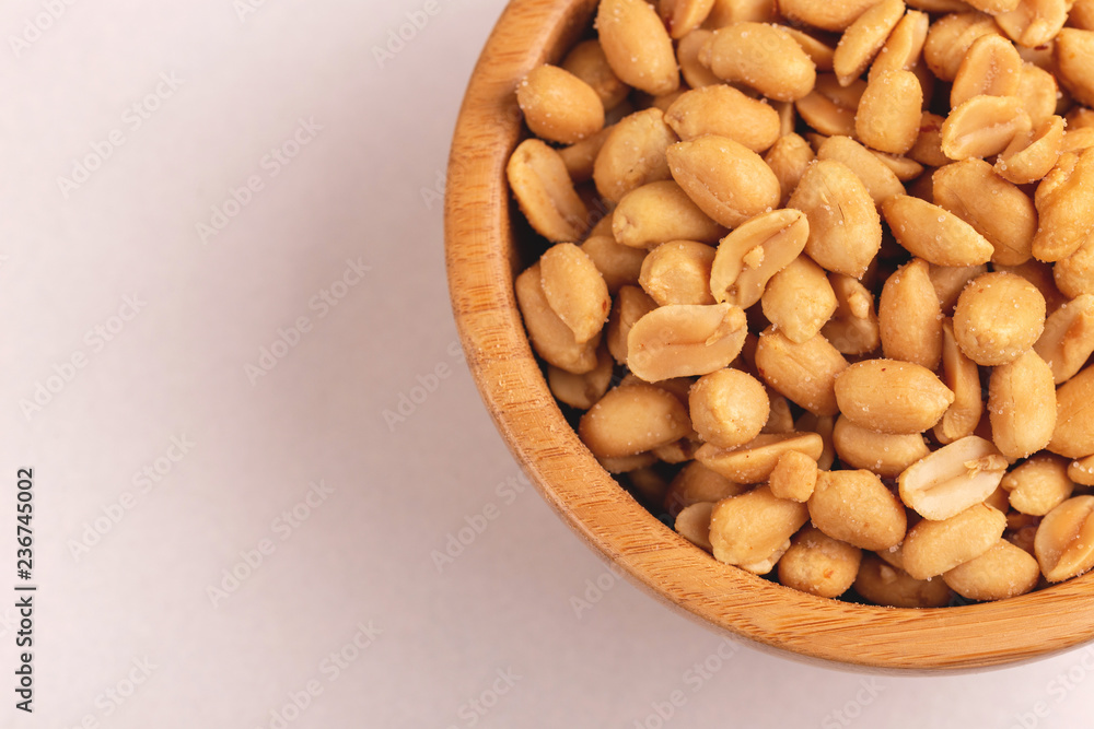 Roasted peanuts in wooden bowl on light marble background Roasted peanuts in wooden bowl on light marble background